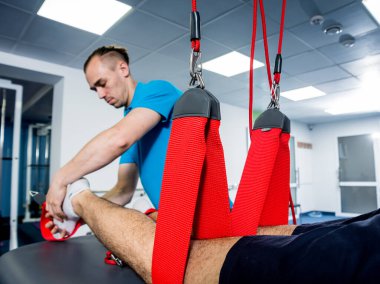 Fizyoterapi. Uzaklaştırma eğitim terapisi. Genç adam süspansiyon temelli egzersiz sistemiyle fitness çekiş terapisi yapıyor.