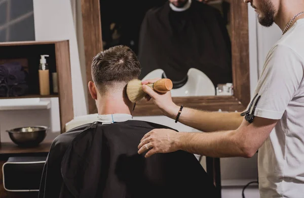 Young man with trendy haircut at barber shop. Barber does the hairstyle and beard trim. Concept barbershop.