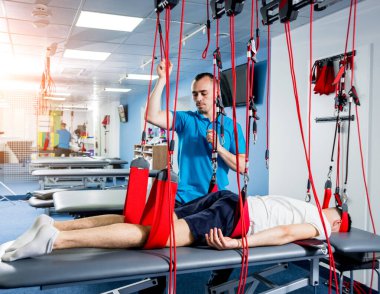 Fizyoterapi. Uzaklaştırma eğitim terapisi. Genç adam süspansiyon temelli egzersiz sistemiyle fitness çekiş terapisi yapıyor.