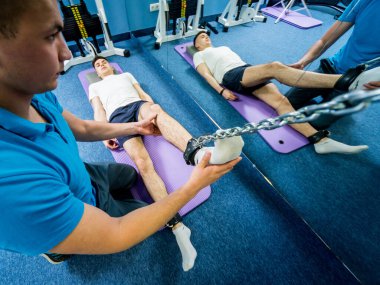 Rehabilitasyon terapisi. Fizyoterapistin gözetiminde paspas üzerinde egzersiz yapan genç bir adam. Omurgada tedavi ağrısı