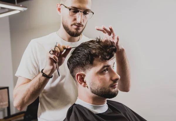Young man with trendy haircut at barber shop. Barber does the hairstyle and beard trim. Concept barbershop.