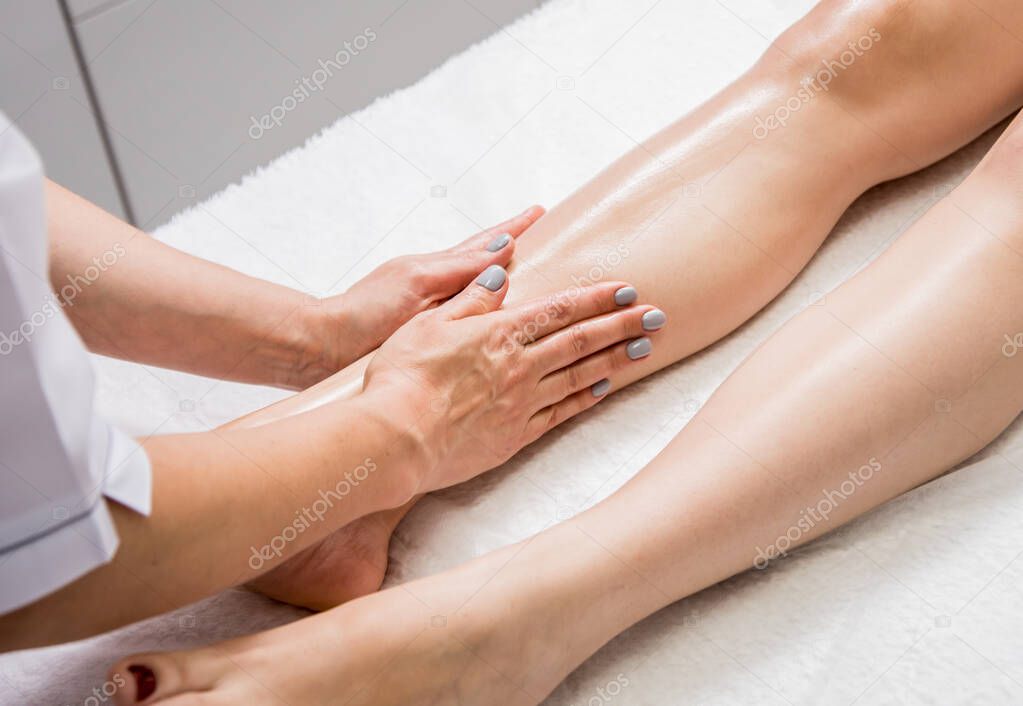 Beautiful young woman enjoying legs massage in spa salon. Cosmetology concept