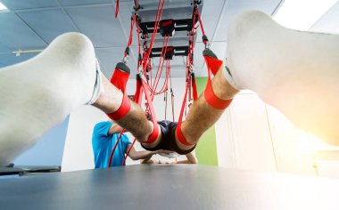 Fizyoterapi. Uzaklaştırma eğitim terapisi. Genç adam süspansiyon temelli egzersiz sistemiyle fitness çekme terapisi yapıyor. Omurgadaki ağrının tedavisi.