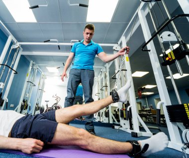 Rehabilitasyon terapisi. Fizyoterapistin gözetiminde paspas üzerinde egzersiz yapan genç bir adam. Omurgada tedavi ağrısı