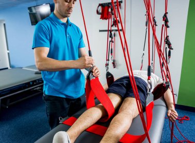 Fizyoterapi. Uzaklaştırma eğitim terapisi. Genç adam süspansiyon temelli egzersiz sistemiyle fitness çekiş terapisi yapıyor.