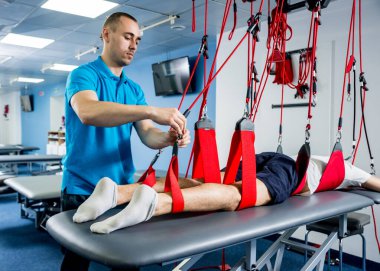 Fizyoterapi. Uzaklaştırma eğitim terapisi. Genç adam süspansiyon temelli egzersiz sistemiyle fitness çekiş terapisi yapıyor.