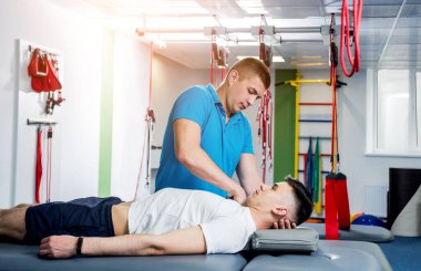 Rehabilitasyon terapisi. Rehabilitasyon merkezinde genç bir erkek hastayla çalışan fizyoterapist.
