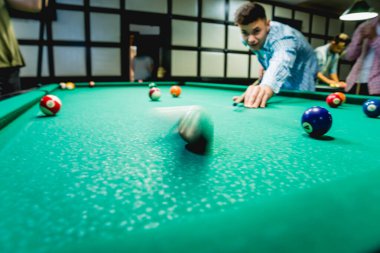 Genç adam bilardoda topa vurmaya çalışıyor. Havuz arkaplanı