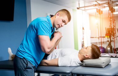 Rehabilitasyon terapisi. Rehabilitasyon merkezinde genç bir erkek hastayla çalışan fizyoterapist.