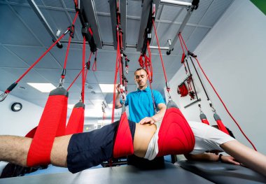 Fizyoterapi. Uzaklaştırma eğitim terapisi. Genç adam süspansiyon temelli egzersiz sistemiyle fitness çekiş terapisi yapıyor.. 