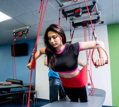 Genç bir kadın süspansiyon temelli egzersiz sistemiyle fitness çekiş terapisi yapıyor. Fizyoterapi kavramı