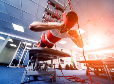 Fizyoterapi. Uzaklaştırma eğitim terapisi. Genç adam süspansiyon temelli egzersiz sistemiyle fitness çekme terapisi yapıyor. Omurgadaki ağrının tedavisi.