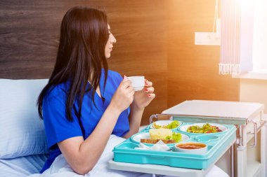 Hastanede yemek yiyen genç bir kadın, hasta için kahvaltı tepsisi.