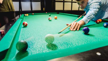 Genç adam bilardoda topa vurmaya çalışıyor. Havuz arkaplanı