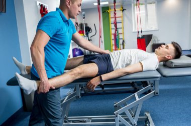 Rehabilitasyon terapisi. Rehabilitasyon merkezinde genç bir erkek hastayla çalışan fizyoterapist.