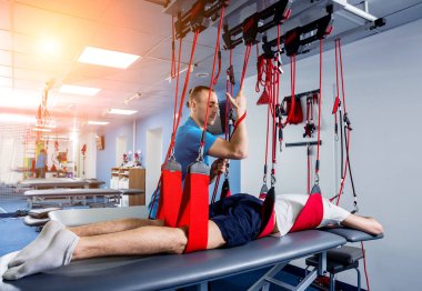 Fizyoterapi. Uzaklaştırma eğitim terapisi. Genç adam süspansiyon temelli egzersiz sistemiyle fitness çekiş terapisi yapıyor.