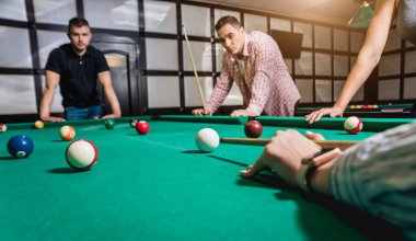 Genç adam bilardoda topa vurmaya çalışıyor. Havuz arkaplanı