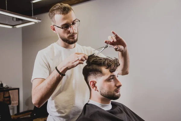 Young man with trendy haircut at barber shop. Barber does the hairstyle and beard trim. Concept barbershop.