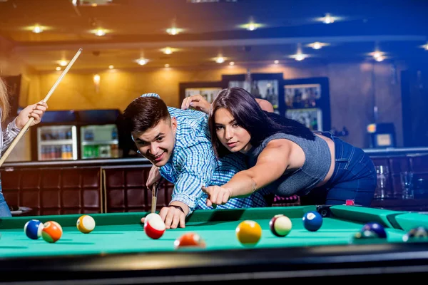 Group of young cheerful friends playing billiards. Funny time after work