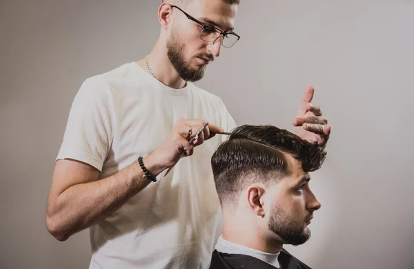 Young man with trendy haircut at barber shop. Barber does the hairstyle and beard trim. Concept barbershop.