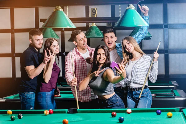 Un grupo de amigos hace una selfie en la mesa de billar. Posando con un taco en sus manos . —  Fotos de Stock