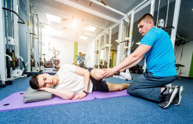 Rehabilitasyon terapisi. Fizyoterapistin gözetiminde paspas üzerinde egzersiz yapan genç bir adam. Omurgada tedavi ağrısı