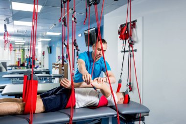 Fizyoterapi. Uzaklaştırma eğitim terapisi. Genç adam süspansiyon temelli egzersiz sistemiyle fitness çekiş terapisi yapıyor.