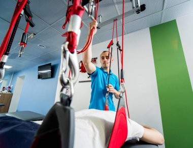 Fizyoterapi. Uzaklaştırma eğitim terapisi. Genç adam süspansiyon temelli egzersiz sistemiyle fitness çekiş terapisi yapıyor.