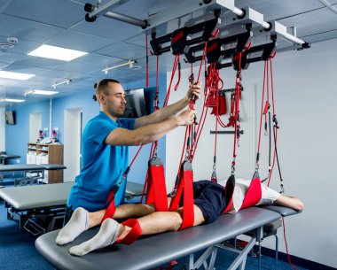 Fizyoterapi. Uzaklaştırma eğitim terapisi. Genç adam süspansiyon temelli egzersiz sistemiyle fitness çekiş terapisi yapıyor.