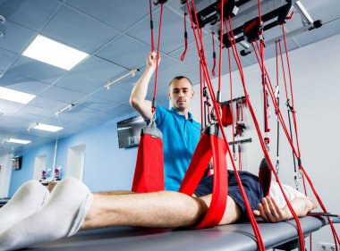 Fizyoterapi. Uzaklaştırma eğitim terapisi. Genç adam süspansiyon temelli egzersiz sistemiyle fitness çekiş terapisi yapıyor.