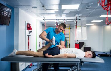 Rehabilitasyon terapisi. Rehabilitasyon merkezinde genç bir erkek hastayla çalışan bir fizyoterapist. Omurgada tedavi ağrısı