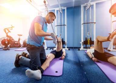 Rehabilitasyon terapisi. Fizyoterapistin gözetiminde paspas üzerinde egzersiz yapan genç bir adam. Omurgada tedavi ağrısı