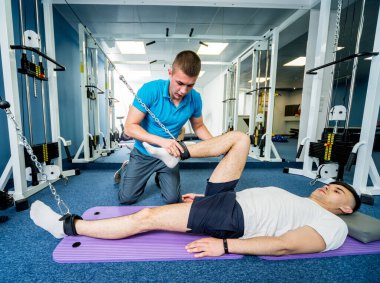 Rehabilitasyon terapisi. Fizyoterapistin gözetiminde paspas üzerinde egzersiz yapan genç bir adam. Omurgada tedavi ağrısı