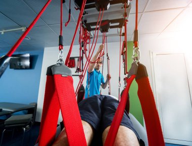 Fizyoterapi. Uzaklaştırma eğitim terapisi. Genç adam süspansiyon temelli egzersiz sistemiyle fitness çekiş terapisi yapıyor.