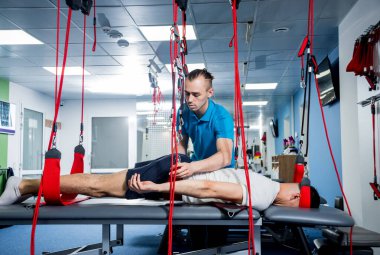 Fizyoterapi. Uzaklaştırma eğitim terapisi. Genç adam süspansiyon temelli egzersiz sistemiyle fitness çekiş terapisi yapıyor.