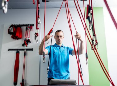 Uzaklaştırma eğitim terapisi. Genç adam süspansiyon temelli egzersiz sistemiyle fitness çekme terapisi yapıyor. Omurgadaki ağrının tedavisi.