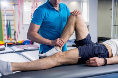 Rehabilitasyon terapisi. Rehabilitasyon merkezinde genç bir erkek hastayla çalışan fizyoterapist.