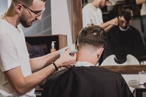 Young man with trendy haircut at barber shop. Barber does the hairstyle and beard trim. Concept barbershop.