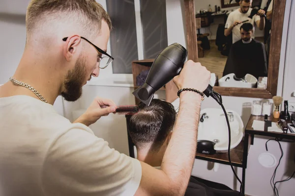 Young man with trendy haircut at barber shop. Barber does the hairstyle and beard trim. Concept barbershop.