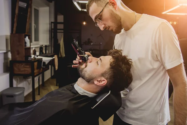 Young man with trendy haircut at barber shop. Barber does the hairstyle and beard trim. Concept barbershop.