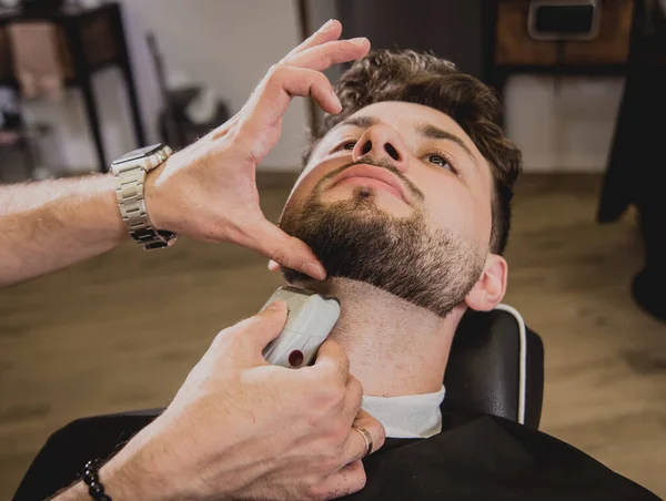 Young man with trendy haircut at barber shop. Barber does the hairstyle and beard trim. Concept barbershop.