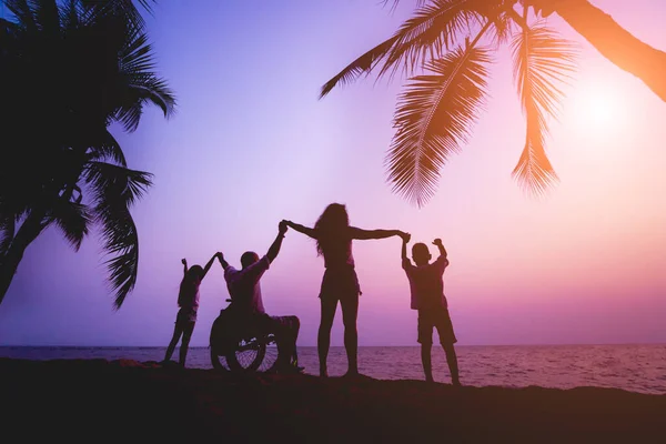 Disabled man in a wheelchair with his family on the beach. Silhouettes at sunset