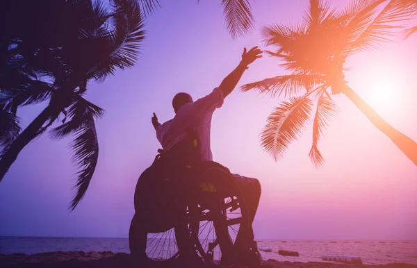 Disabled man in a wheelchair on the beach. Silhouette at sunset. — Stockfoto