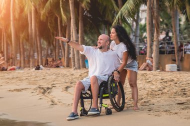 Disabled man in a wheelchair with his wife on the beach.