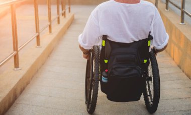 Disabled man in a wheelchair moves on a ramp to the beach.