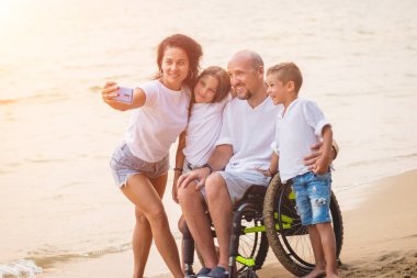 Disabled man in a wheelchair with his family on the beach.