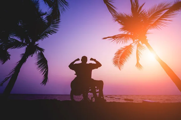 Disabled man in a wheelchair on the beach. Silhouette at sunset. — ストック写真