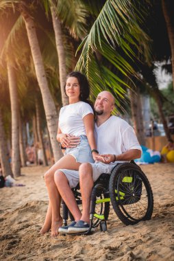 Disabled man in a wheelchair with his wife on the beach.
