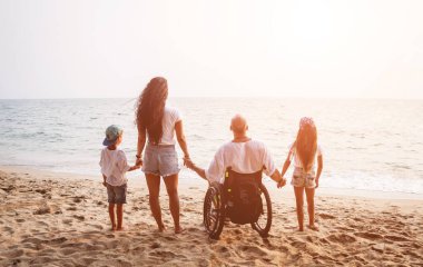Disabled man in a wheelchair with his family on the beach.