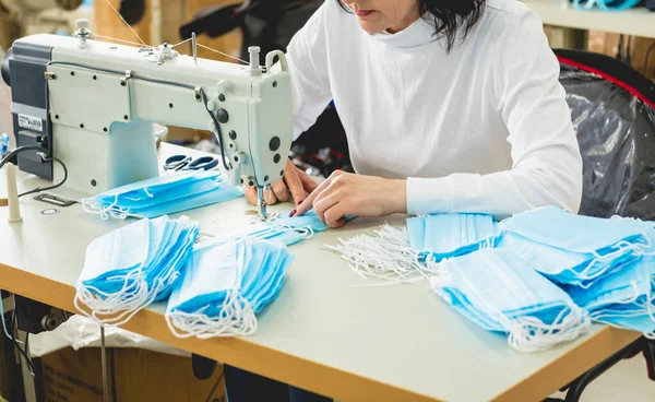 Žena šije ošetřovatelku obličeje na šicím stroji. Koronavirová pandemie. — Stock fotografie